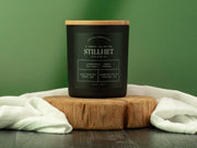 Black candle with wooden lid on a wooden block against a green background